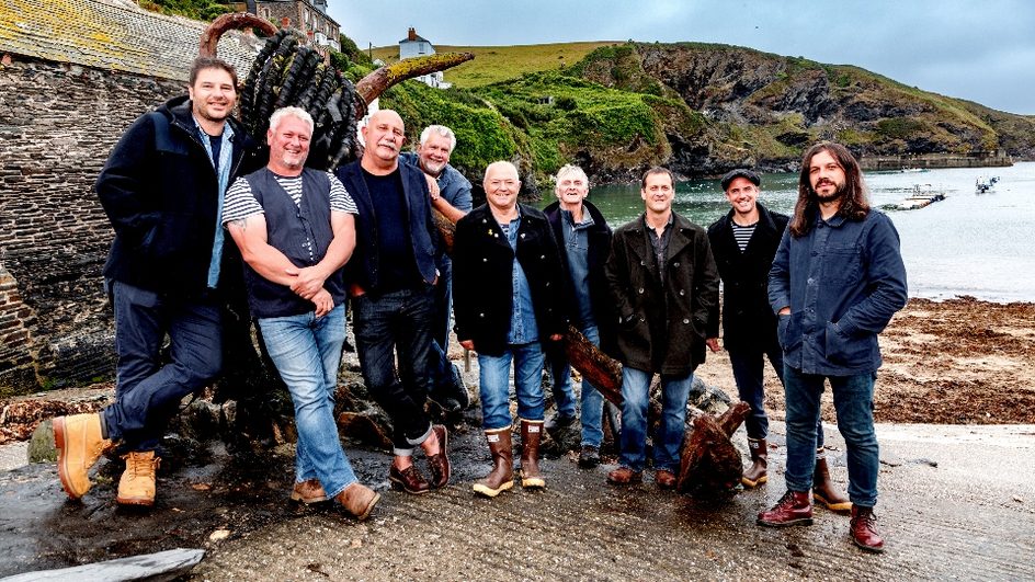 Fisherman's Friends standing on the beach in a line.